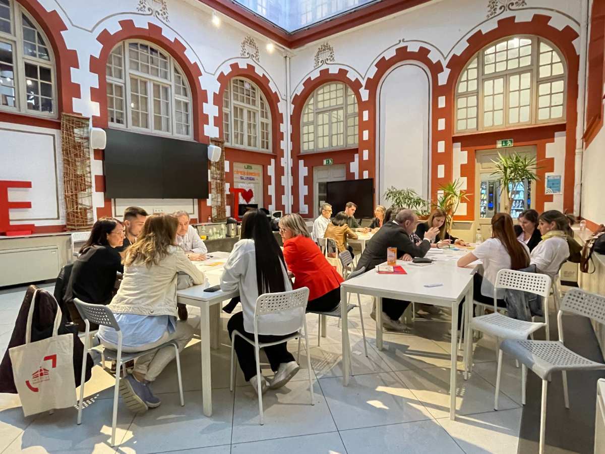 Tres grupos de personas reunidas en torno a una mesa, dos en primer término y la última al fondo