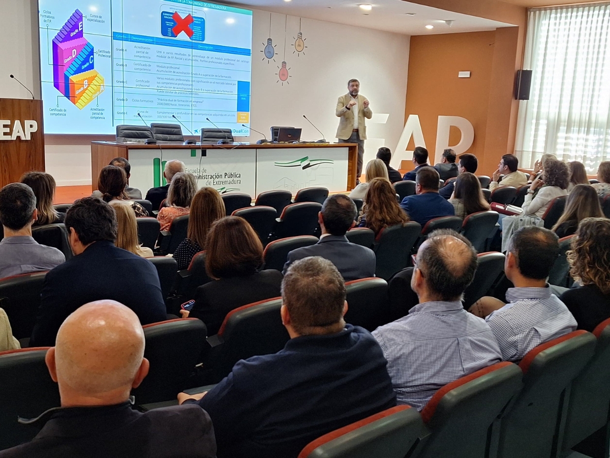 Personas asistiendo a una ponencia en un salón de actos, fotografiadas desde atrás, con la proyección de una tabla un unos gráficos al fondo